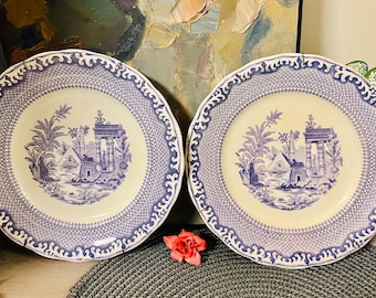 May include: Two vintage blue and white porcelain plates with a decorative border and a central design of a blue and white scene with palm trees and a building.
