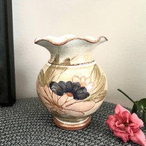 May include: A small, hand-painted ceramic vase with a scalloped rim. The vase is decorated with a floral pattern in shades of pink, green, blue, and brown.