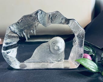 May include: A clear glass paperweight featuring a sculpted seal inside a mountain-shaped frame.