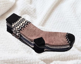 Puede incluir: Una pila de calcetines cálidos en varios colores, incluyendo gris, azul y rosa. Cada calcetín tiene un talón y una puntera negros, con un diseño estampado en el puño. Los calcetines están colocados sobre una superficie blanca y texturizada.