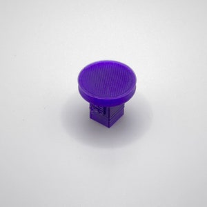 May include: A small, purple, 3D printed object with a round top and a square base.
