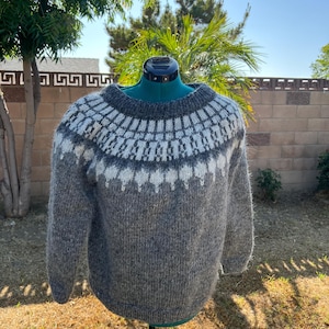 May include: A gray and white patterned sweater with a round neckline. The sweater has a geometric design around the yoke and upper chest. The body of the sweater is a solid gray color. The sweater is displayed on a mannequin.