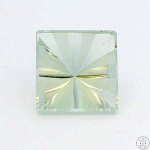 May include: A square-cut, pale green gemstone with a starburst pattern carved into its surface. The gemstone is set against a white background, showcasing its clarity and intricate design. The facets catch the light, creating a sparkling effect.