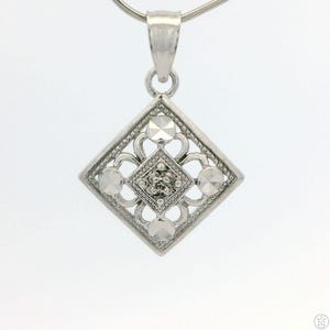 May include: A silver pendant with a diamond-shaped design. The pendant features a central cluster of small stones surrounded by four larger, faceted stones. The design is set within a diamond-shaped frame with an open filigree pattern. The pendant hangs from a silver chain.
