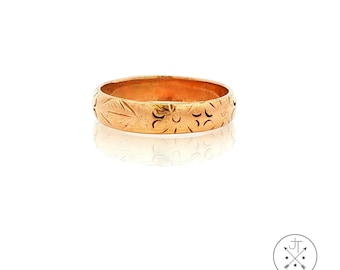 May include: A gold-toned metal band ring featuring a repeating engraved pattern of small leaves and circular floral motifs around the entire outer circumference of the band. The ring has a smooth, polished finish and a consistent width.