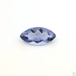 May include: A marquise-cut, faceted gemstone with a light blue hue. The gemstone is set against a white background, showcasing its polished surfaces and internal facets. The elongated shape and color suggest it could be a tanzanite or similar precious stone.