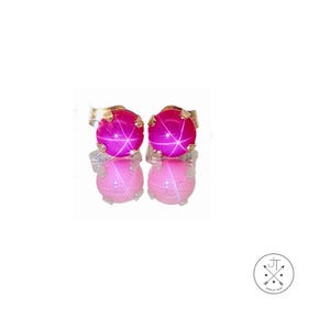 May include: A pair of stud earrings featuring vibrant pink star-shaped gemstones. The earrings have a gold setting and are displayed on a reflective surface, showcasing their color and design. The jewelry is a classic accessory.