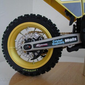 Könnte beinhalten: Ein gelbes und schwarzes Dirtbike mit einem schwarzen Reifen und einer gelben Felge. Das Fahrrad hat eine silberne Kette und eine silberne Schwinge mit dem Text "Original Bayerisch Malz" darauf.