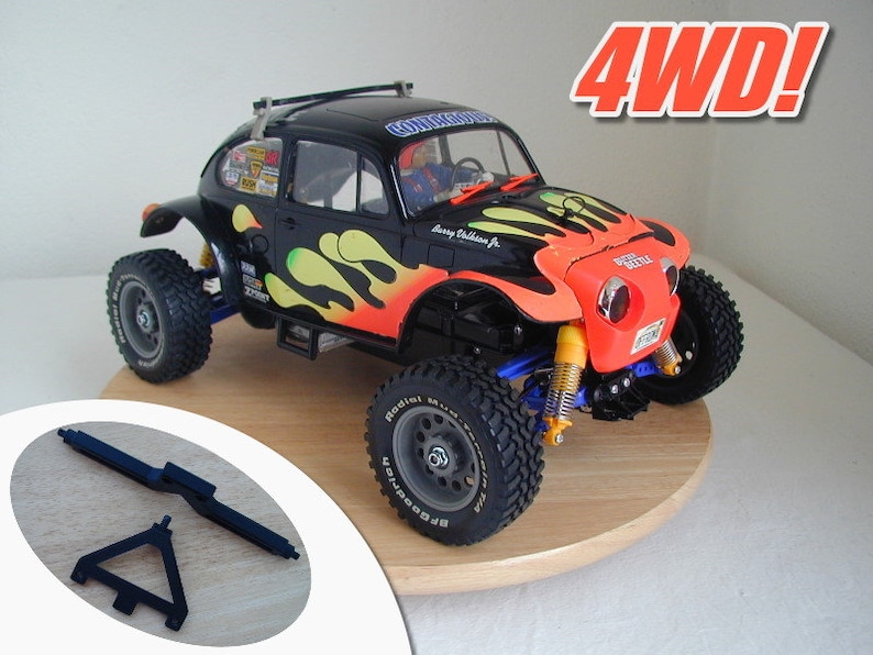 May include: A black and orange 4WD radio-controlled car with a yellow and orange flame design. The car has a roll cage and a spare tire mounted on the back. The car is sitting on a wooden base. The text "4WD!" is in red letters on a white background.