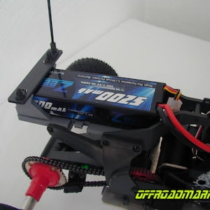 Può includere: Primo piano del telaio nero e grigio di un'auto telecomandata con una batteria blu e nera con l'etichetta "5200mAh". L'auto ha un'antenna nera, fili rossi e neri e un componente di ingranaggio rosso.
