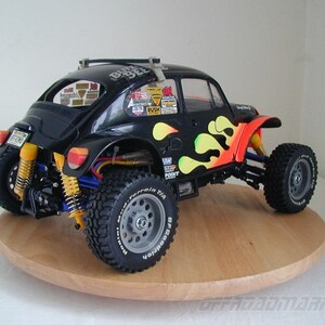 May include: Black and yellow radio-controlled car model of a Volkswagen Beetle with flames painted on the side. The car is on a wooden turntable. The car has a roll cage and off-road tires.