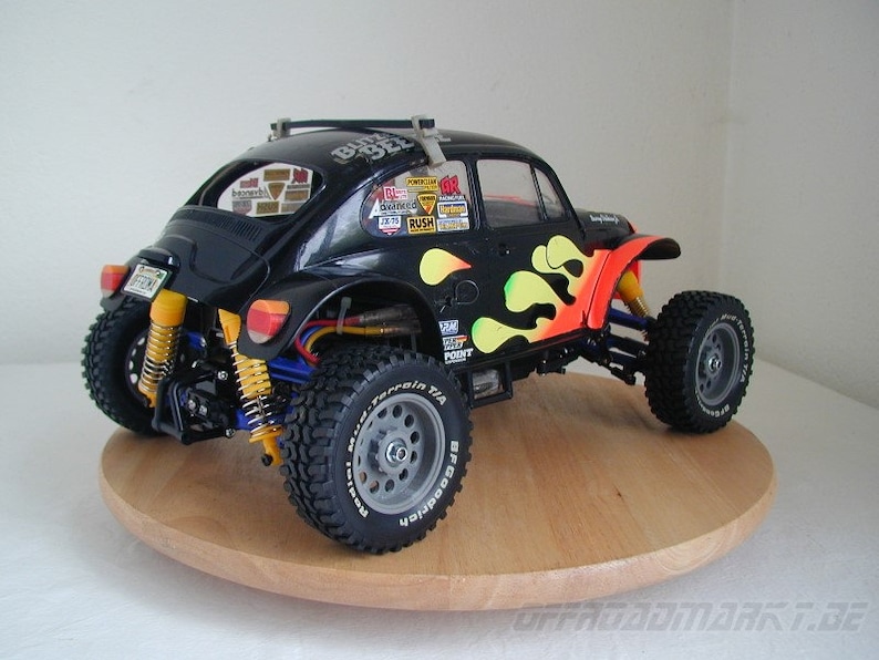 May include: Black and yellow radio-controlled car model of a Volkswagen Beetle with flames painted on the side. The car is on a wooden turntable. The car has a roll cage and off-road tires.