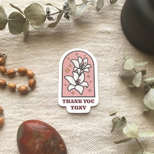May include: Pink sticker with a white flower illustration and the text "Thank You Tony" in brown lettering.