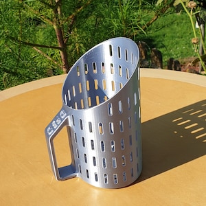 Peut inclure: Une louche en métal argenté avec une poignée et un design perforé. La louche est posée sur une surface en bois.