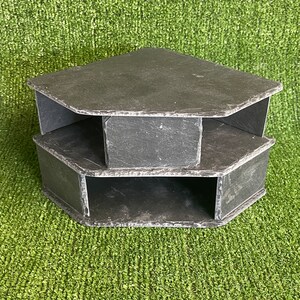 May include: A three-tiered corner shelf made of dark grey slate. Each shelf has a unique shape and is designed to fit in a corner.