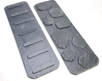 May include: Two rectangular dark gray slate boards. One board features six horizontal rectangular slate strips attached to its surface. The second board features seven irregular, rounded slate pieces attached to its surface.
