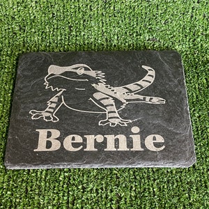 May include: Black slate stone with a white engraved image of a bearded dragon and the name "Bernie" underneath.