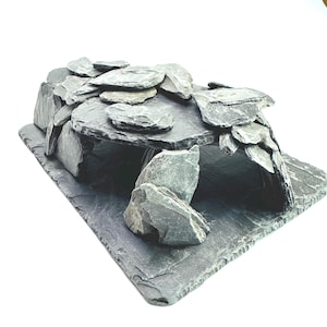 May include: A dark grey slate stone structure featuring a flat rectangular base with multiple layered, jagged rock pieces arranged to form a hollow cave-like enclosure. The natural stone has a textured, layered appearance with varying shades of grey.