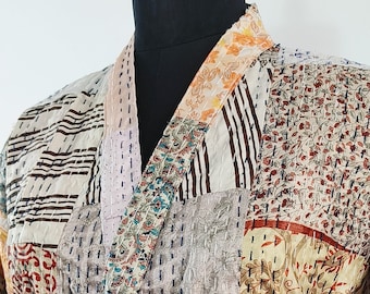 Puede incluir: Una bata kimono de patchwork con una variedad de patrones florales y geométricos en tonos marrones, beige, rosa, verde y morado. La bata tiene un cinturón de lazo y mangas largas.