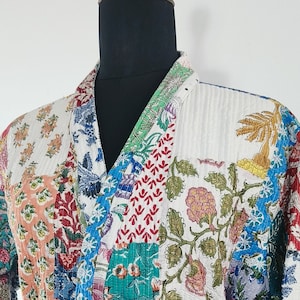 May include: A white quilted robe with a colorful patchwork design featuring floral patterns in shades of blue, green, red, yellow, and pink. The robe has a tie belt and long sleeves.