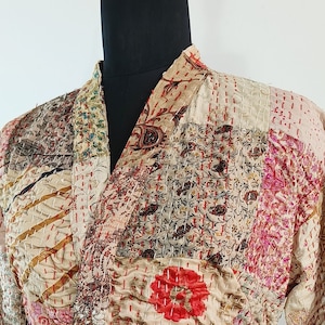 May include: A long-sleeved robe made from patchwork fabric in shades of beige, brown, pink, and red. The robe has a tie belt and is quilted with intricate stitching.