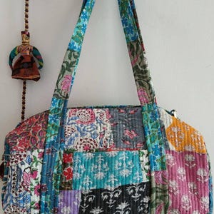 May include: A patchwork quilted tote bag with a variety of floral patterns in shades of blue, pink, green, and yellow. The bag has two top handles and a zipper closure.