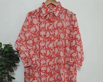 May include: A long-sleeved shirt dress in a bright red colour, decorated with a white floral design. The dress has a traditional collar and a loose fit, suitable for everyday wear. The material seems light and airy.