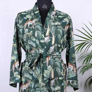 May include: A dark green robe with a jungle-themed pattern featuring leopards, monkeys, and tropical foliage. The robe has a white trim and a matching belt. It is displayed on a mannequin.