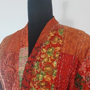 May include: A red, orange, and green patchwork robe with a floral pattern. The robe has a tie belt and a pocket on the left side.