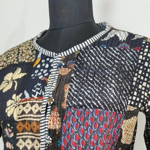Peut inclure: Une veste à manches longues présentant un motif patchwork avec divers panneaux de tissu noirs, rouges, bleus et crème. Le vêtement possède une encolure ronde, une fermeture à boutons sur le devant et une bordure rayée noire et blanche.