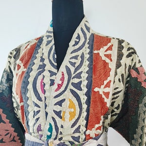 Könnte beinhalten: Eine farbenfrohe, gemusterte Jacke im Kimono-Stil mit einem Bindegürtel. Die Jacke besteht aus einem Patchwork aus verschiedenen Stoffen und zeigt eine Vielzahl von geometrischen und floralen Mustern in Rot-, Blau-, Grün-, Gelb- und Weißtönen.