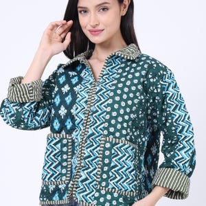 Op de afbeelding: Een gewatteerde jas in tinten van teal, wit en blauw met een geometrisch patroon. De jas heeft een kraag, zakken en gestreepte manchetten. De jas is open en toont de binnenvoering.