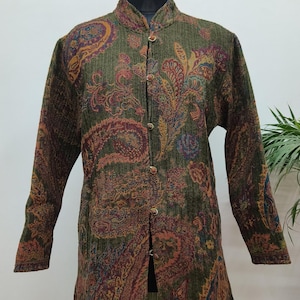 Op de afbeelding: Een lange, olijfgroene jas met een paisley patroon in tinten rood, oranje en blauw. De jas heeft een opstaande kraag en is aan de voorkant dichtgeknoopt. De jas wordt op een paspop getoond.