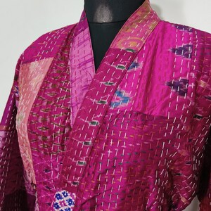 May include: A magenta kimono-style robe with a patchwork design. The robe has a wrap-around belt and is decorated with white stitching. The fabric has a textured appearance, and the design includes various patterns and colours.