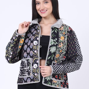 May include: A patchwork jacket with a black base and floral patterns in various colours. The jacket has a collared neckline, long sleeves, and a striped trim. Sunglasses rest on top of the head.