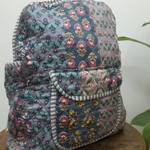 May include: A patchwork quilted backpack with a floral print in shades of blue, pink, and green. The backpack has a large main compartment and a smaller front pocket.