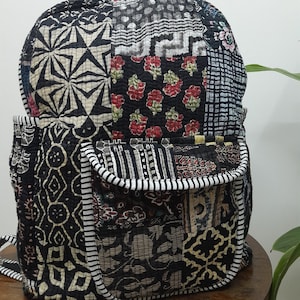 May include: A black and white patchwork backpack with a large front pocket. The backpack is made of quilted fabric with various patterns, including floral, geometric, and abstract designs.