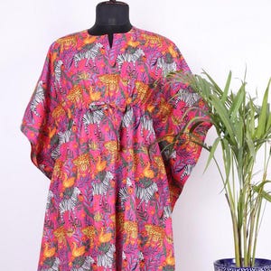 May include: A pink maxi dress with a zebra, leopard, and bird print. The dress has a V-neck and a tie at the waist.