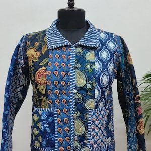 May include: A quilted jacket with a patchwork design. The jacket features a variety of blue floral and paisley patterns, with a striped collar and trim. The jacket is displayed on a black mannequin.