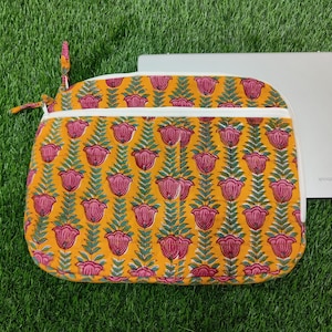 May include: A yellow laptop sleeve with a pink floral pattern. The sleeve has a white zipper and a white lining.