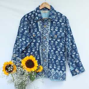 Può includere: Una giacca di cotone blu e bianco con motivo, con chiusura a bottoni e due tasche. La giacca ha una fodera a righe bianche e blu.