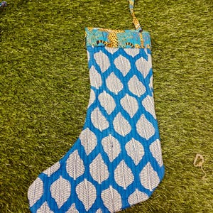May include: A blue and white leaf-patterned Christmas stocking with a patterned cuff and hanging loop. The stocking is made of fabric and is designed for holiday decor.
