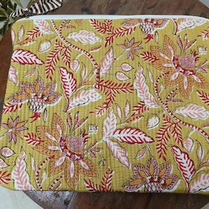 May include: A yellow quilted fabric pouch with a floral print in shades of red, pink, and orange. The pouch has a white zipper.