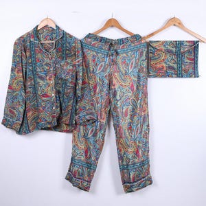 Puede incluir: Un conjunto de pijama de tres piezas con un colorido estampado de cachemira. El conjunto incluye una camisa con botones, pantalones con cordón y una bolsa a juego. La tela presenta una mezcla de tonos azules, rojos y amarillos.