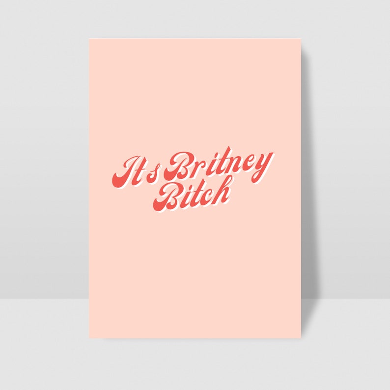 以下が含まれることがあります： ピンクの背景に、赤い筆記体で「It's Britney, Bitch」というテキストが書かれています。