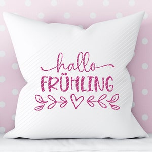 K&ouml;nnte beinhalten: Wei&szlig;es Kissen mit rosa Schriftzug "hallo FR&Uuml;HLING" mit einem rosa Herz und einem Blattdesign.