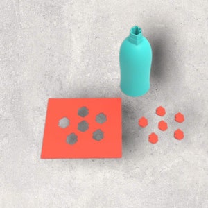 May include: A teal bottle-shaped object, a bright orange square with six gray cutouts, and eight small orange flower-shaped objects are arranged on a gray surface. The bottle has a unique, textured top.