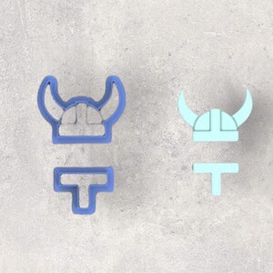 May include: Two cookie cutters, one blue and one light blue, shaped like a Viking helmet with horns and a separate piece for the axe.