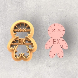 May include: Two voodoo doll cookie cutters, one in orange and one in pink. The orange cutter is a detailed outline of a voodoo doll with stitched eyes and the word "EX" on the chest. The pink cutter is a solid shape of a voodoo doll with stitched eyes and the word "EX" on the chest.