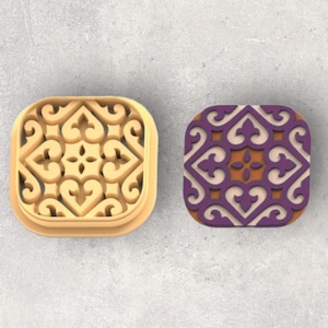 Puede incluir: Dos azulejos cuadrados de cerámica con un intrincado patrón geométrico. Un azulejo es beige con un diseño blanco, y el otro es morado con un diseño blanco y naranja.